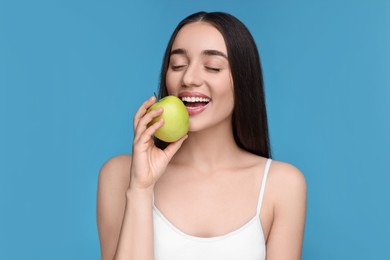 Beautiful young woman with apple on light blue background