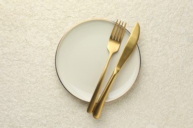 Stylish setting with cutlery and plate on light textured table, top view