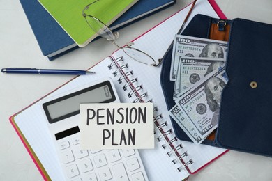 Photo of Card with phrase Pension Plan, dollar banknotes, calculator and notebooks on white office table, flat lay