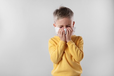Photo of Sick boy with tissue coughing on gray background. Cold symptoms