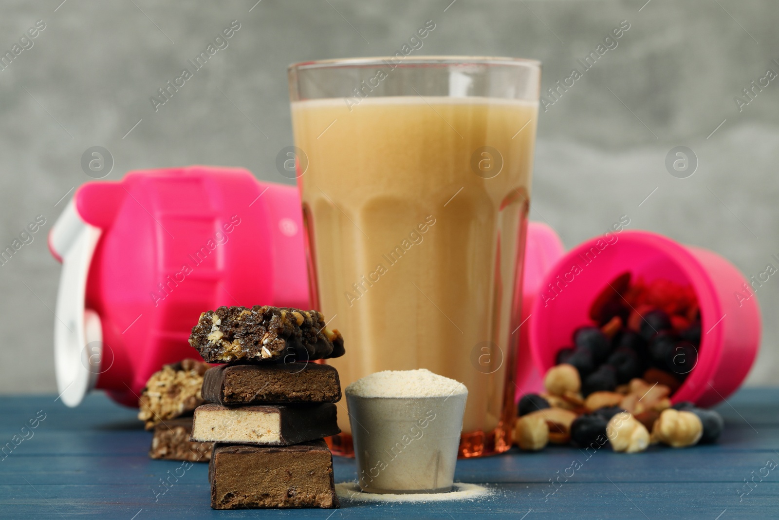 Photo of Different energy bars, protein cocktail and powder on blue wooden table