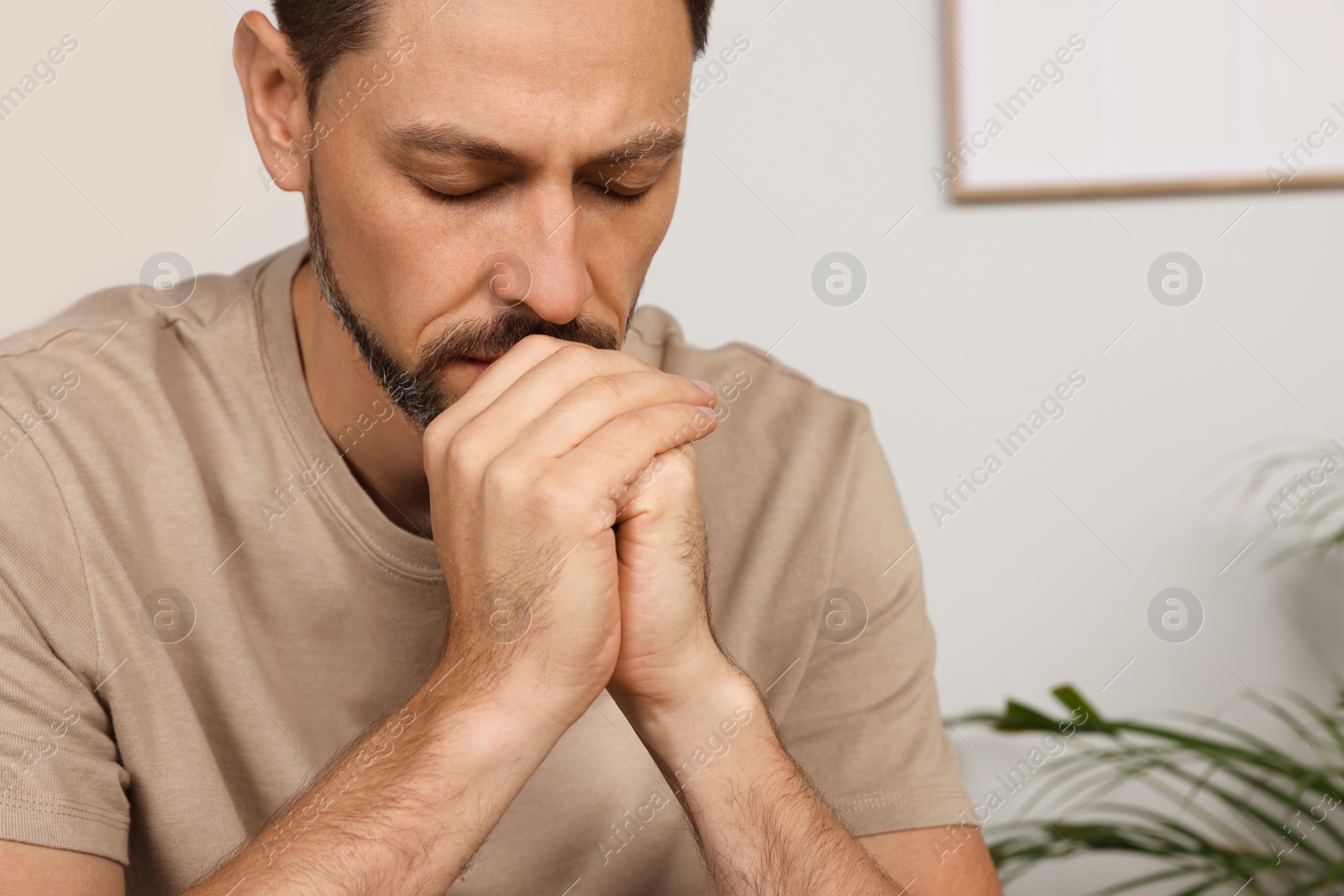 Photo of Man with clasped hands praying in room at home, closeup