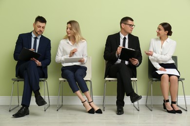 People waiting for job interview near light green wall indoors