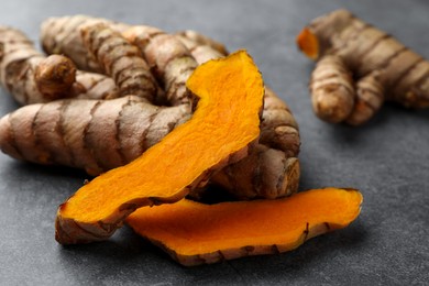 Whole and cut turmeric roots on grey table, closeup