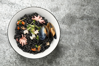 Photo of Delicious black risotto with seafood in bowl on light grey table, top view. Space for text