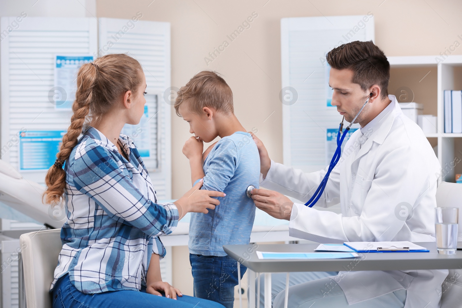 Photo of Doctor examining coughing little boy at clinic