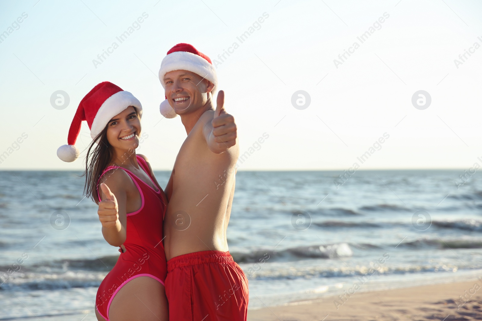 Photo of Happy couple with Santa hats together on beach. Christmas vacation