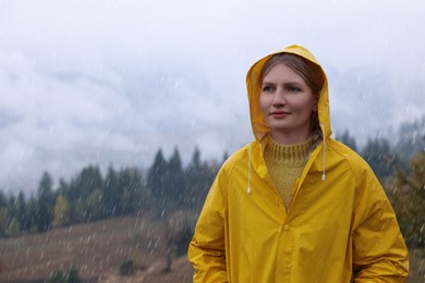 Photo of Young woman in raincoat enjoying mountain landscape under rain