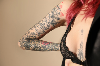 Photo of Beautiful woman with tattoos on body against beige background, closeup