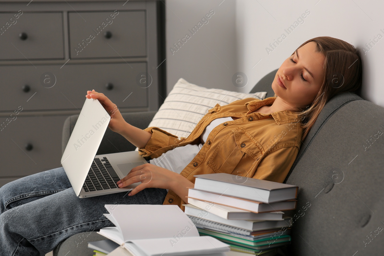 Photo of Young tired woman sleeping near books on couch indoors