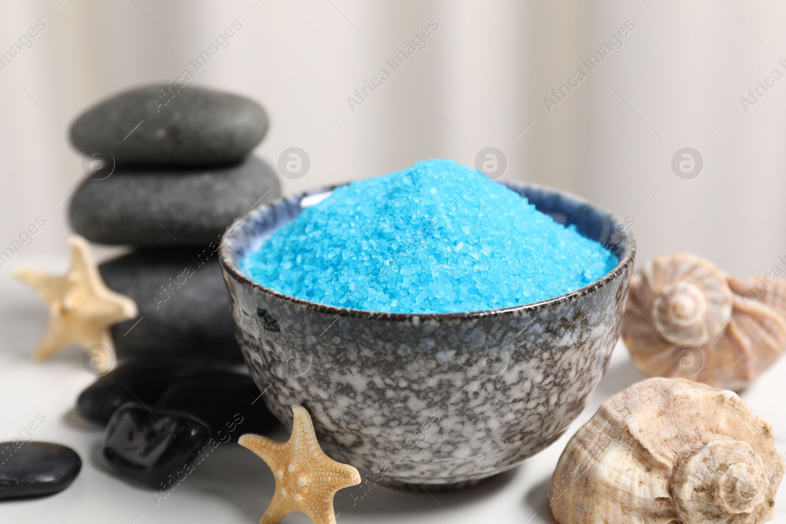 Photo of Light blue sea salt in bowl, spa stones, starfishes and shells on white table, closeup