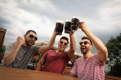 Photo of Friends clinking glasses of beer in outdoor cafe