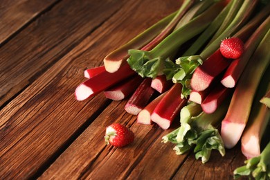 Fresh rhubarb stalks and strawberries on wooden table, space for text