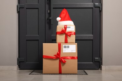 Photo of Christmas gift boxes and Santa hat near door indoors. Sending present by mail