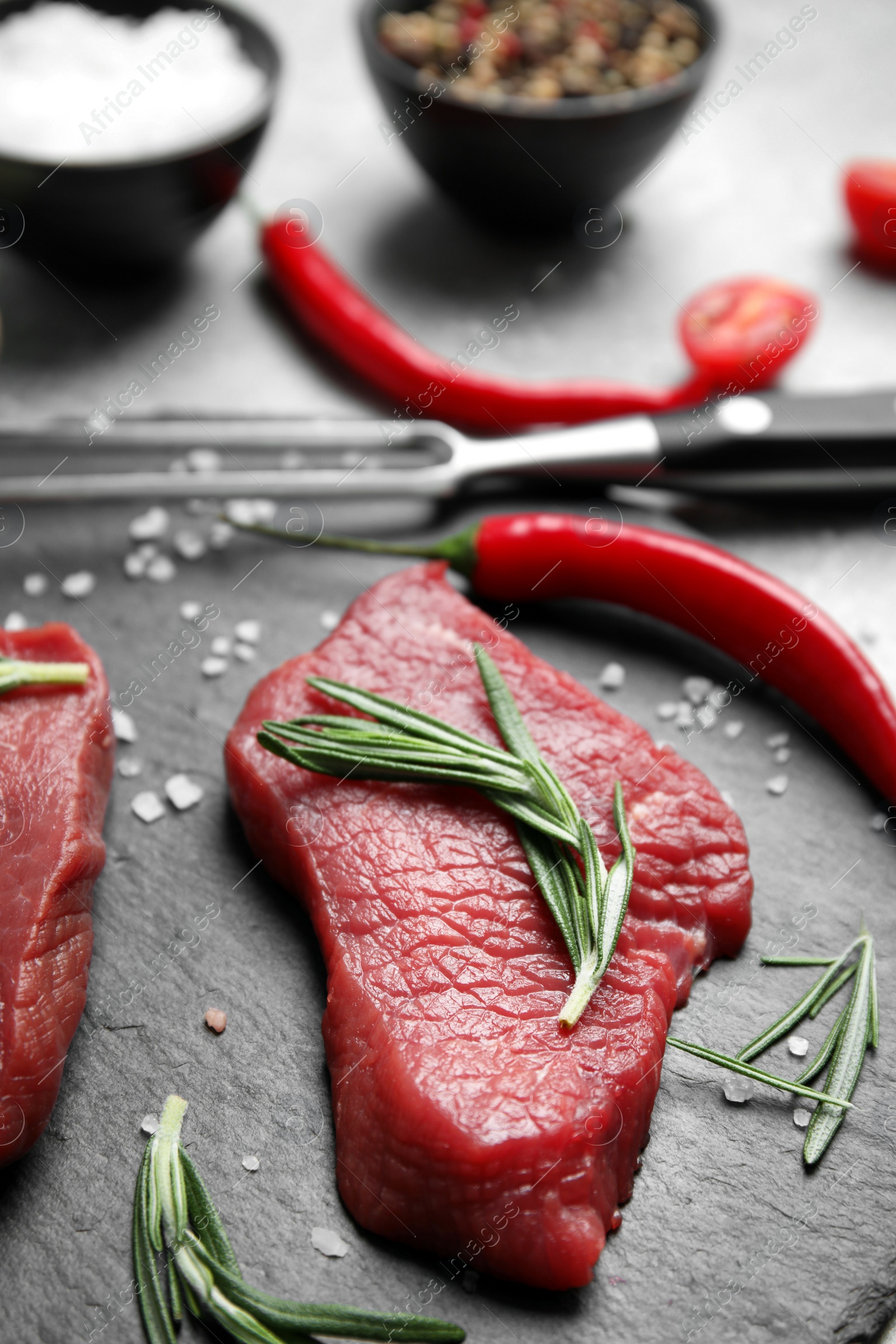 Photo of Fresh raw meat steaks and spices on slate plate, closeup