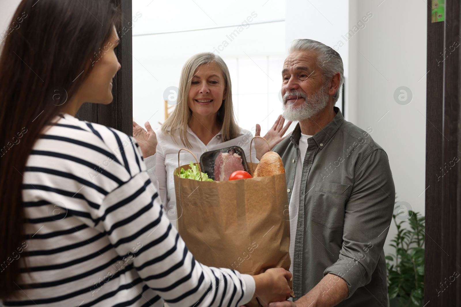 Photo of Courier giving paper bag with food products to senior couple indoors