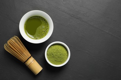 Photo of Cup of fresh matcha tea, green powder and bamboo whisk on black table, flat lay. Space for text