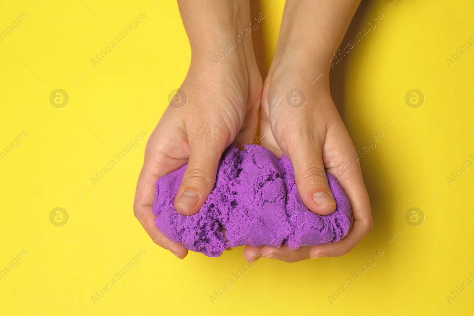 Photo of Woman playing with kinetic sand on yellow background, top view