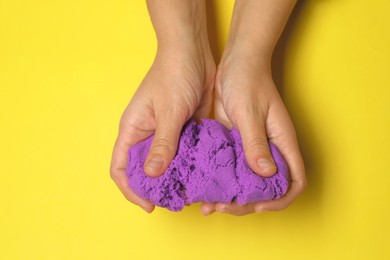 Woman playing with kinetic sand on yellow background, top view