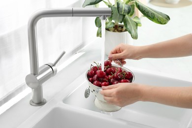 Photo of Woman washing fresh ripe cherries under tap water in kitchen, closeup
