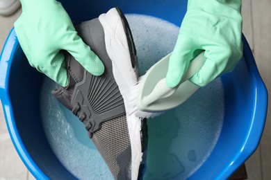 Photo of Woman with gloves and brush cleaning stylish sneakers in wash basin, top view