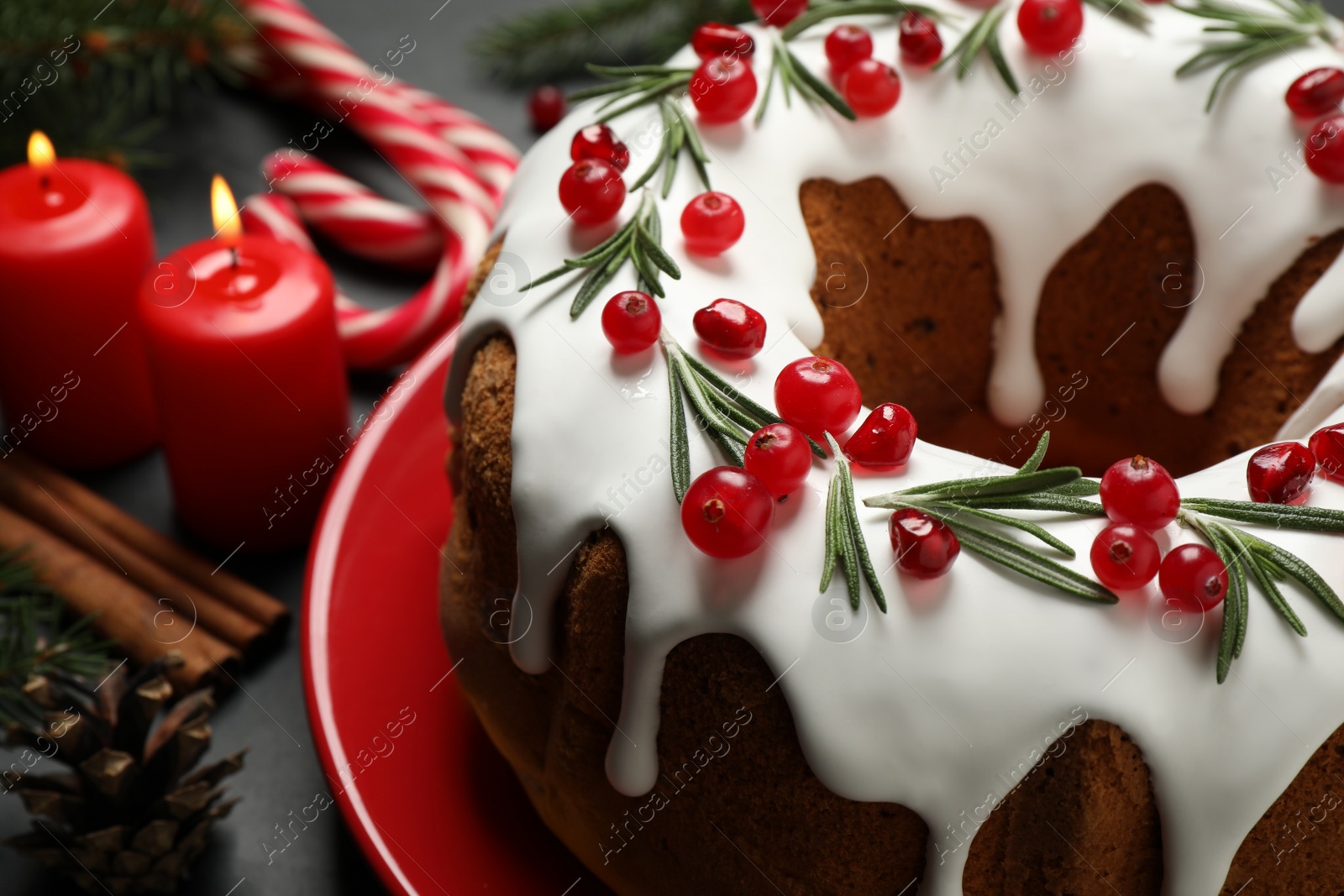 Photo of Traditional Christmas cake decorated with glaze, pomegranate seeds, cranberries and rosemary on dark grey table, closeup