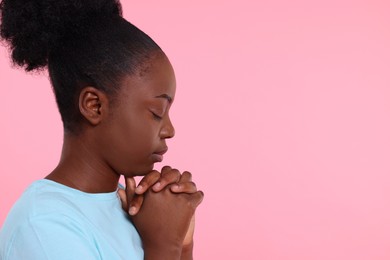 Photo of Woman with clasped hands praying to God on pink background. Space for text