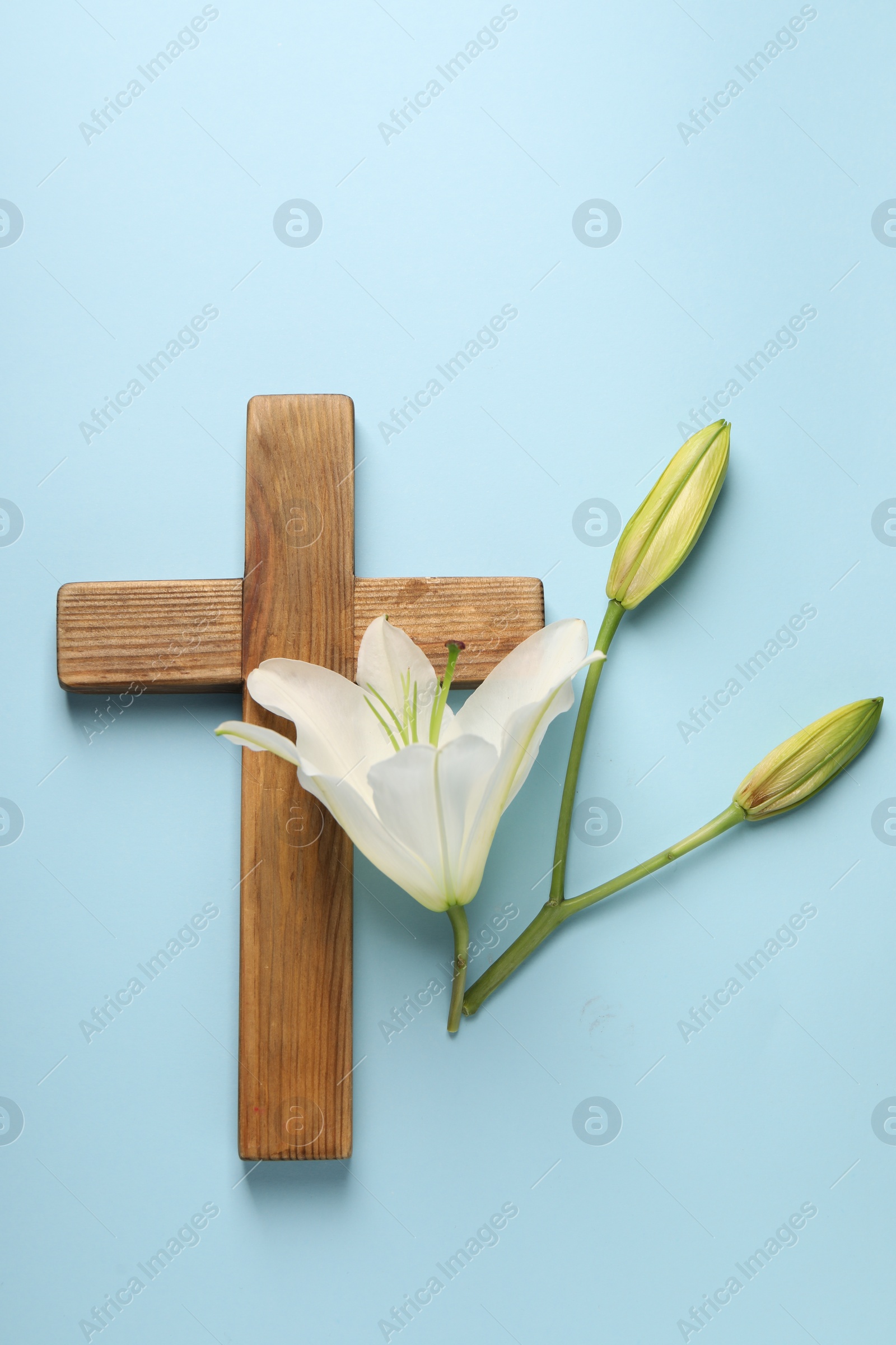 Photo of Wooden cross and lily flowers on light blue background, top view. Easter attributes