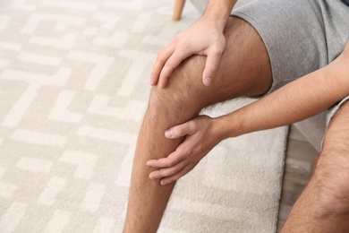 Man suffering from leg pain at home, closeup. Space for text