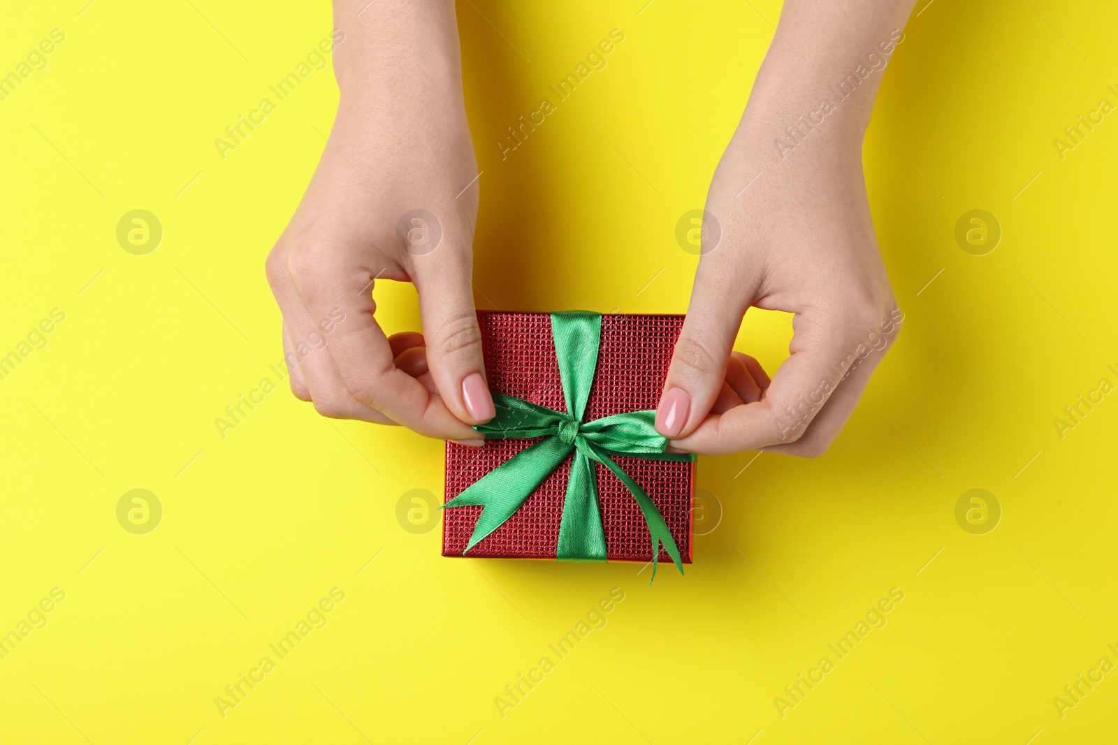 Photo of Woman decorating gift box on yellow background, top view. Christmas present