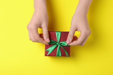 Woman decorating gift box on yellow background, top view. Christmas present