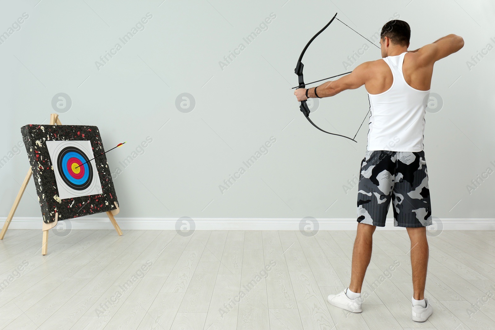 Photo of Man with bow and arrow aiming at archery target indoors