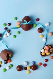 Frame made of tasty chocolate eggs and different candies on light blue background, flat lay with space for text