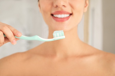 Photo of Woman holding toothbrush with paste indoors, closeup