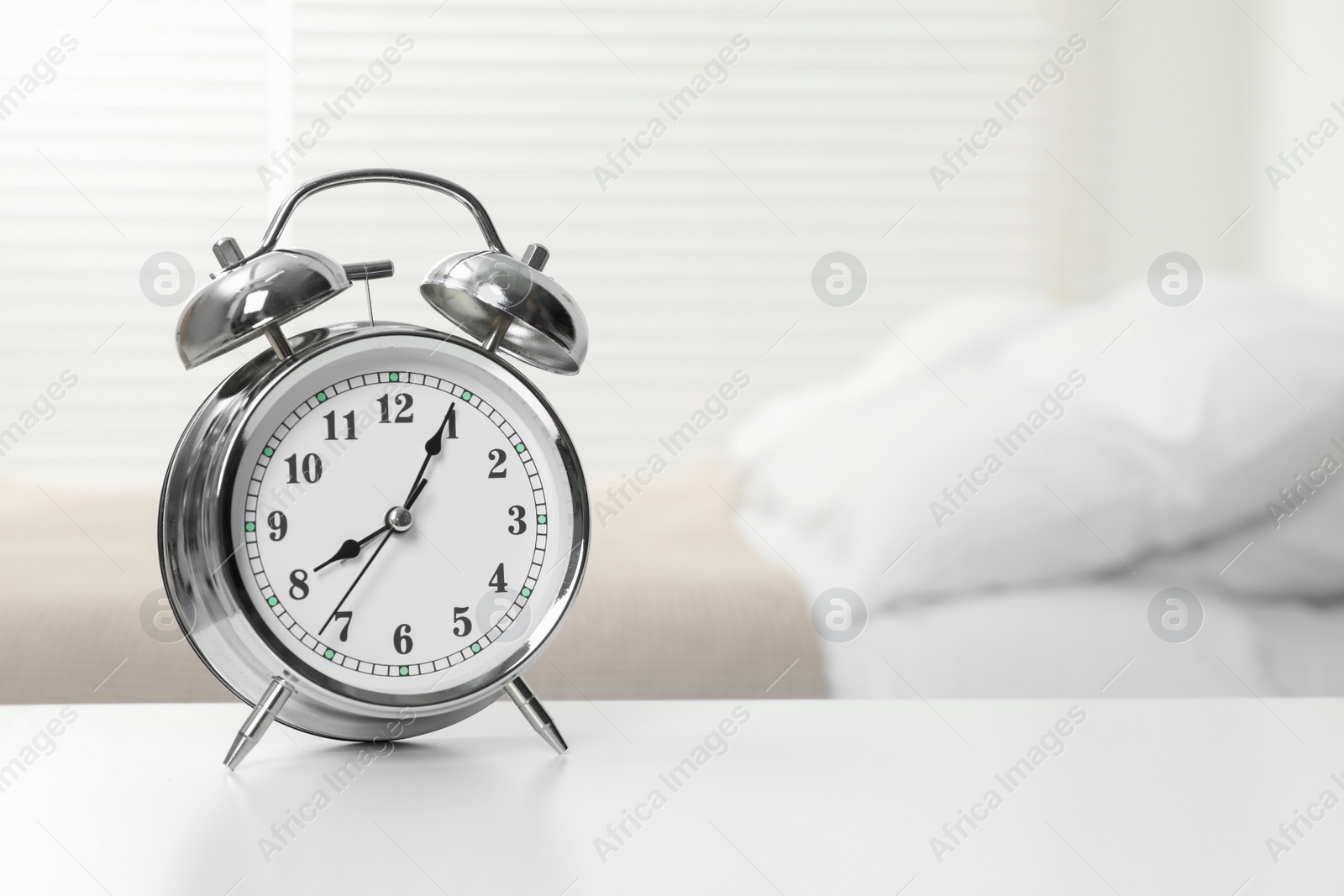 Photo of Silver alarm clock on white wooden table in bedroom, space for text