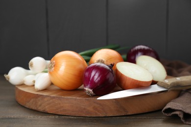 Photo of Board with different kinds of onions on wooden table, closeup