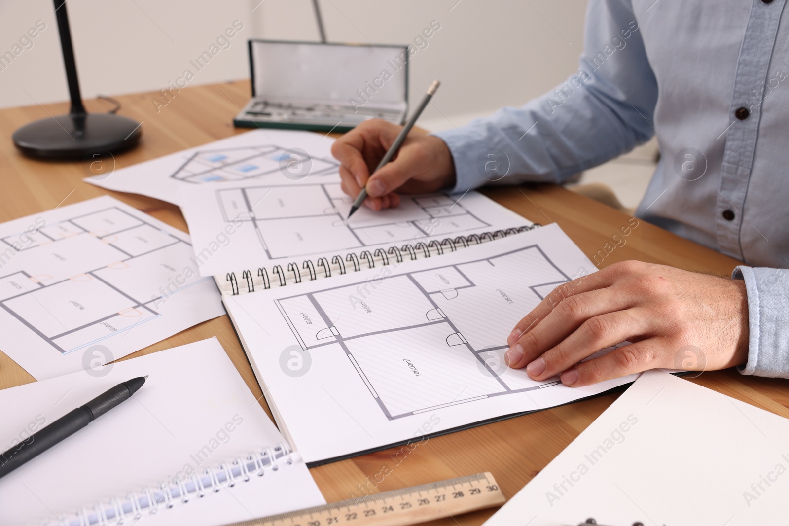 Photo of Man drawing in sketchbook with pencil at wooden table, closeup