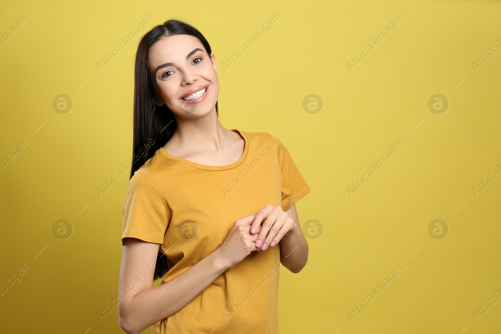 Photo of Portrait of happy young woman with beautiful black hair and charming smile on yellow background, space for text