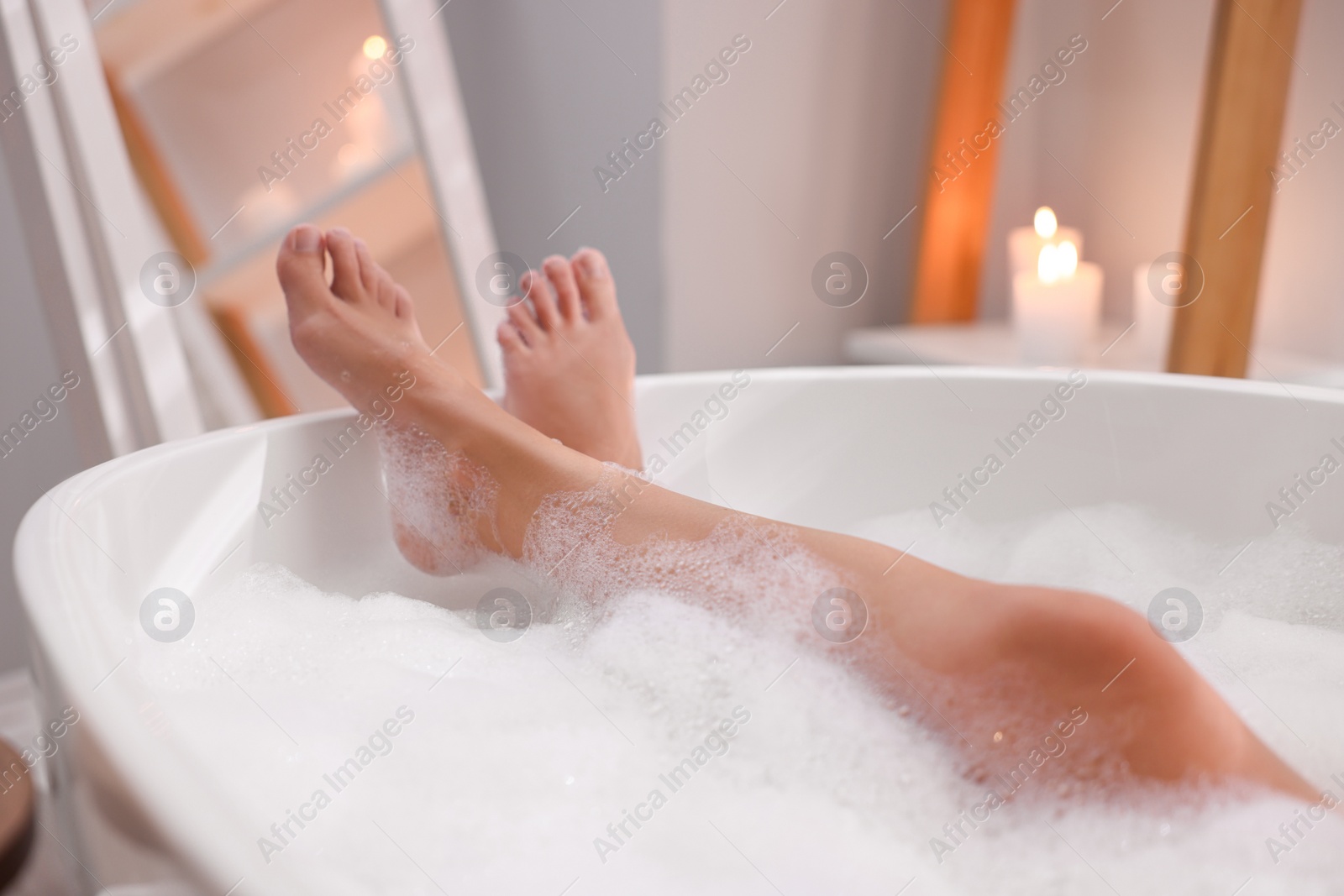 Photo of Woman taking bath in tub with foam indoors, closeup