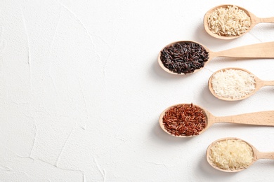 Photo of Flat lay composition with brown and other types of rice in spoons on white background. Space for text