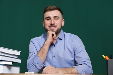 Portrait of young teacher at table against green background