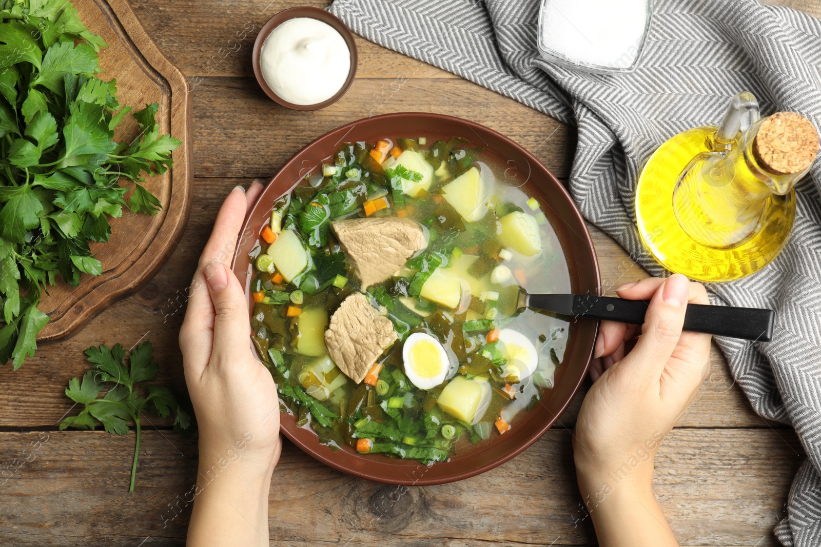 Photo of Woman eating delicious sorrel soup with meat and egg at wooden table, top view