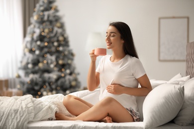 Happy pregnant woman on bed in room decorated for Christmas. Expecting baby