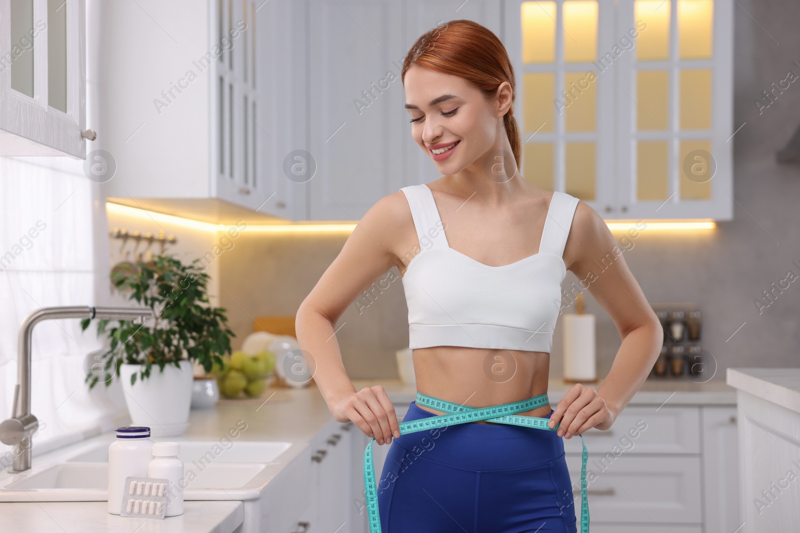 Photo of Slim woman measuring waist with tape in kitchen. Weight loss