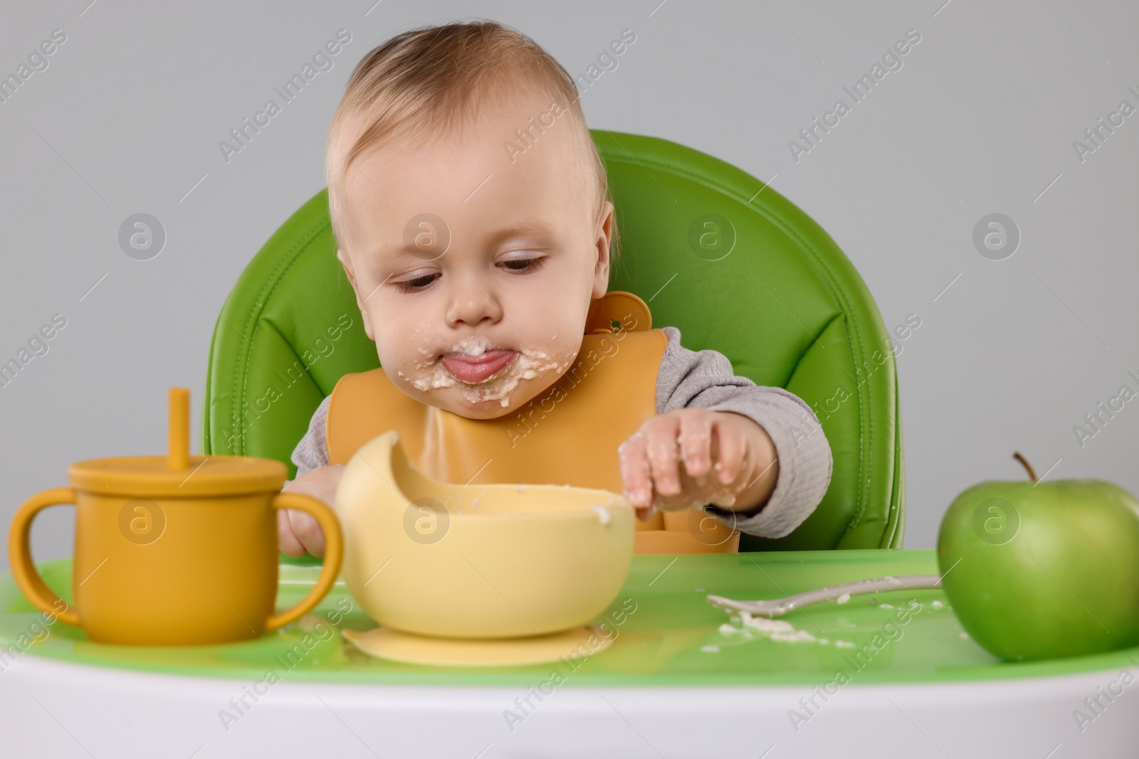 Photo of Cute little baby eating healthy food in high chair on gray background