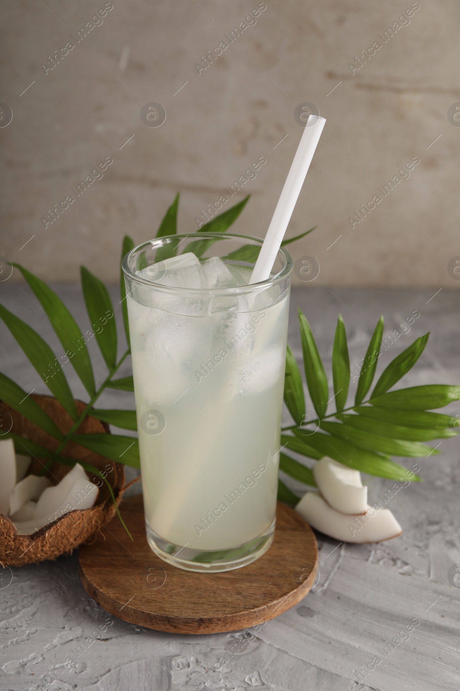 Photo of Glass of coconut water, ice cubes, leaves and nuts on grey table