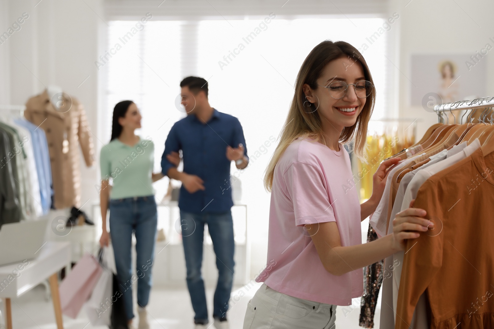 Photo of Young woman choosing clothes near rack in modern boutique