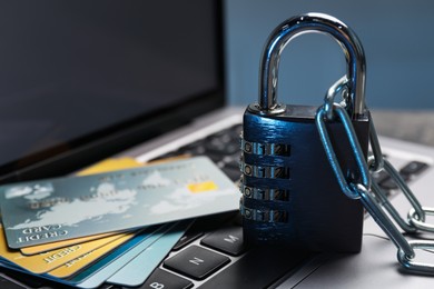 Photo of Cyber security. Metal combination padlock with chain and credit cards on laptop, closeup