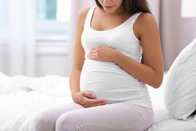 Photo of Happy pregnant woman sitting on bed at home, closeup