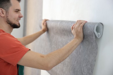 Man hanging stylish gray wallpaper in room
